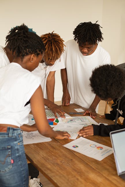 A diverse group of young adults brainstorming ideas over charts and graphs on a wooden table.